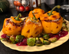 Orange bell peppers carved like jack-o'-lanterns, stuffed with plant-based ground, rice and vegan cheese, with roasted Brussels sprouts