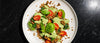 Two halves of a roasted sweet potato loaded with Italian plant-based ground, wilted spinach and cherry tomatoes, drizzled with creamy green goddess dressing