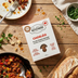 The Better Butchers Chorizo plant-based ground box on a wooden board beside a cooked skillet dish.