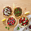 Four plant-based lahmacun flatbreads topped with The Better Butchers ground, red onion, cucumber, tomato, and parsley, served with lemon and sumac